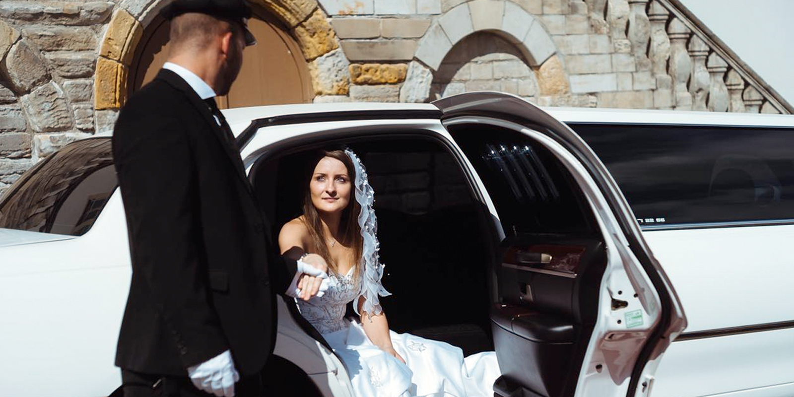 Chauffeur hilft Braut beim aussteigen aus weisser Miet-Limousine in Halle